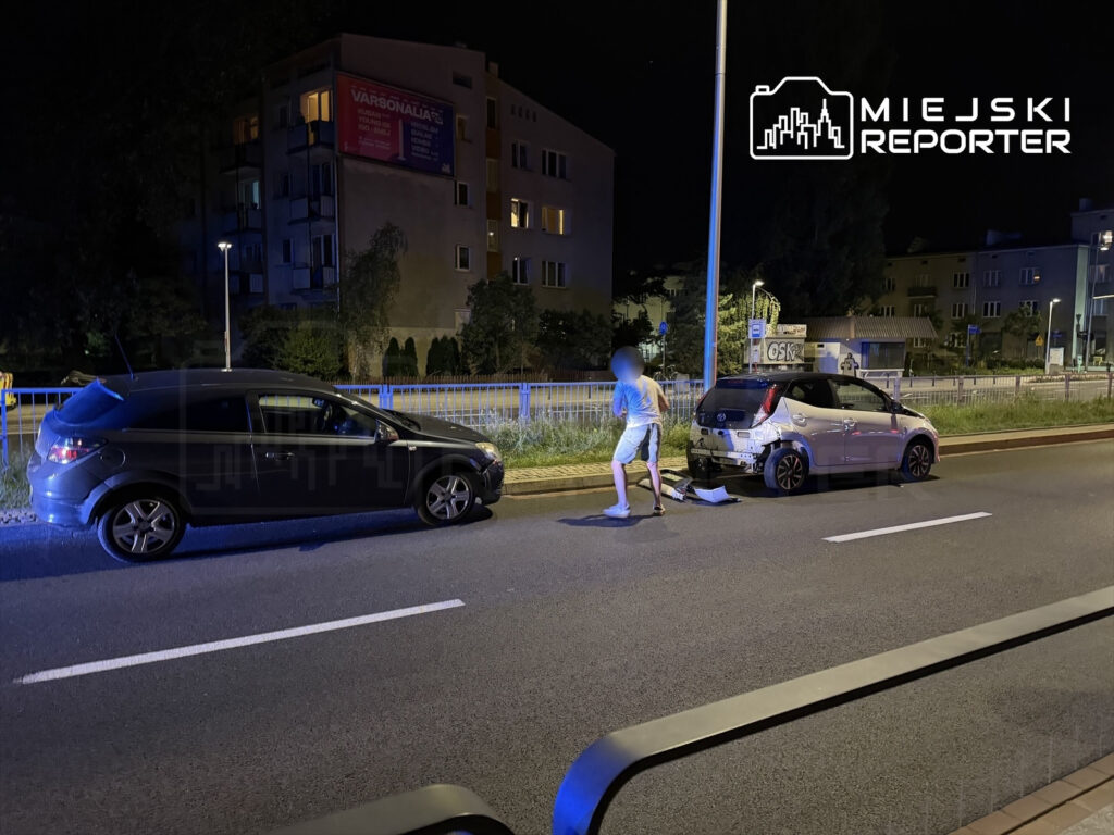 Mężczyzna w szortach ogląda uszkodzenia dwóch samochodów po nocnym zderzeniu na ulicy w miejskim otoczeniu.