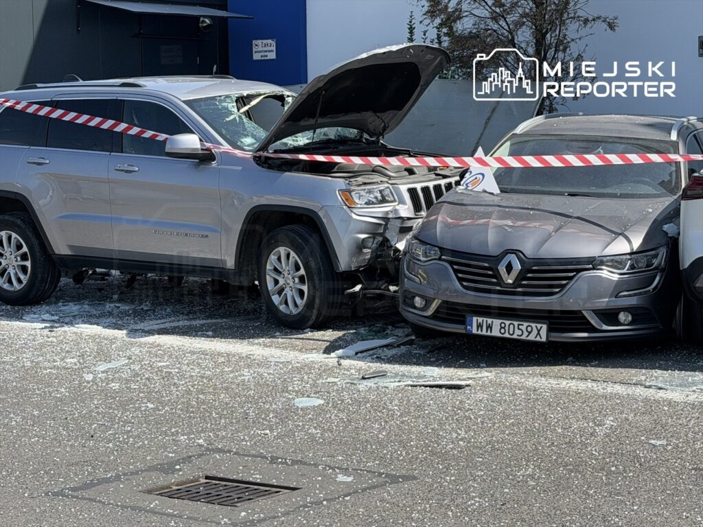 Srebrny SUV z otwartą maską stoi obok uszkodzonego samochodu osobowego, a na ziemi leżą odłamki szkła.