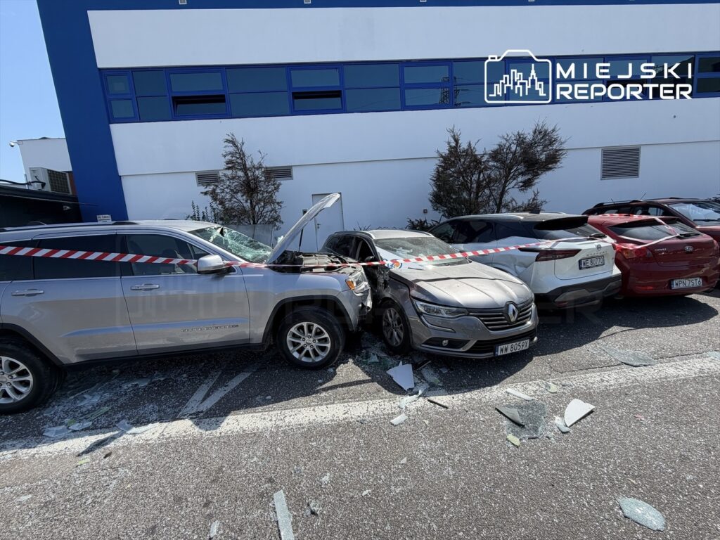 Srebrny SUV z otwartą maską stoi na parkingu, uszkadzając dwa inne samochody, wśród rozbitego szkła i taśm policyjnych.