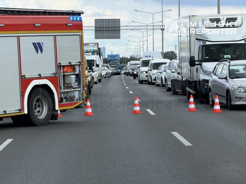 Wozidło strażackie z włączonymi sygnałami świetlnymi blokuje ruch na drodze, a pojazdy stoją w korku.