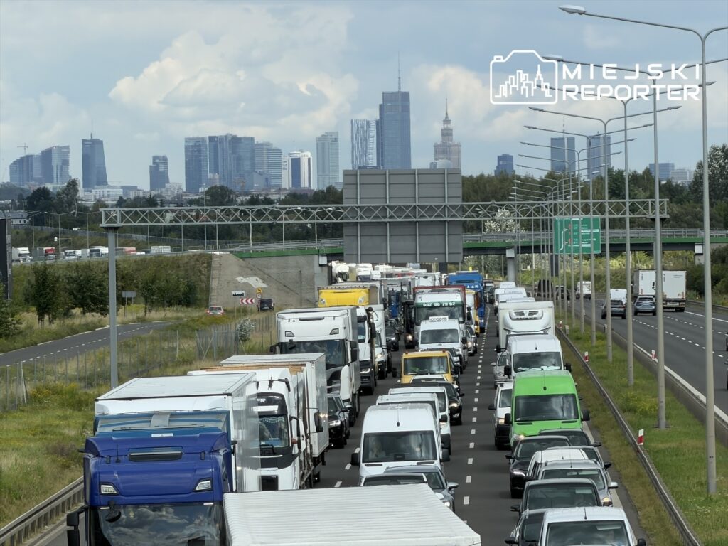 Korki drogowe złożone z ciężarówek i samochodów osobowych na autostradzie z widokiem na skyline miasta.