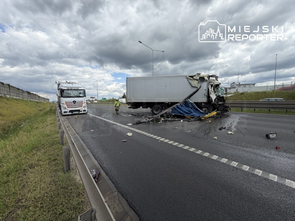 W wyniku wypadku ciężarówka z uszkodzoną kabiną stoi na poboczu drogi, obok pracuje strażak.