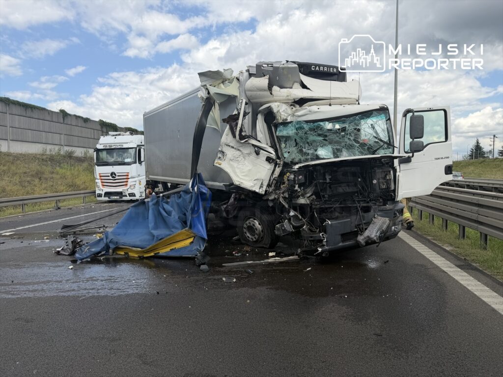 Zniszczony ciężarówka z rozbitym przodem leży na drodze, obok stoi drugi pojazd ciężarowy.