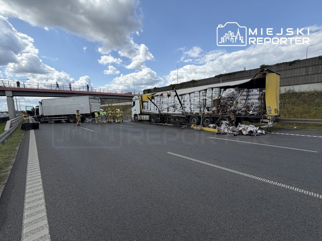 Na autostradzie zderzenie dwóch ciężarówek, wokół pracują strażacy i ratownicy, a towar leży na jezdni.