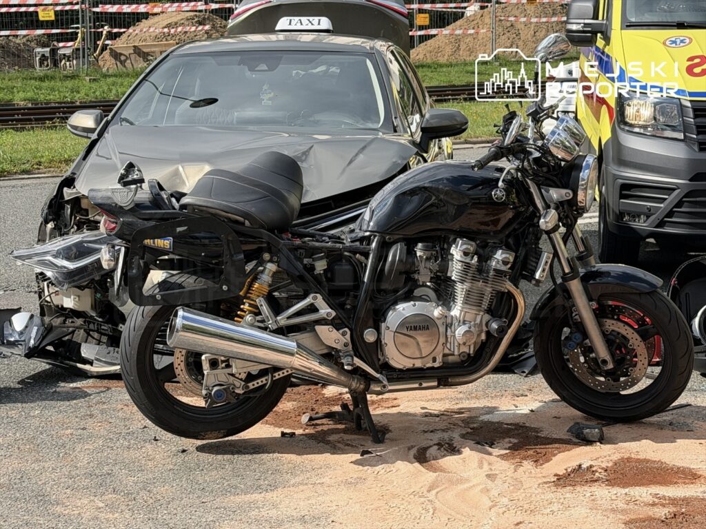 Motocykl marki Yamaha stoi obok uszkodzonego samochodu osobowego, na drodze pokrytej piaskiem.