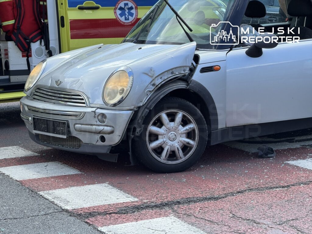 Rozbity samochód osobowy na pasach, obok karetka pogotowia. Na drodze widoczne ślady po stłuczce.