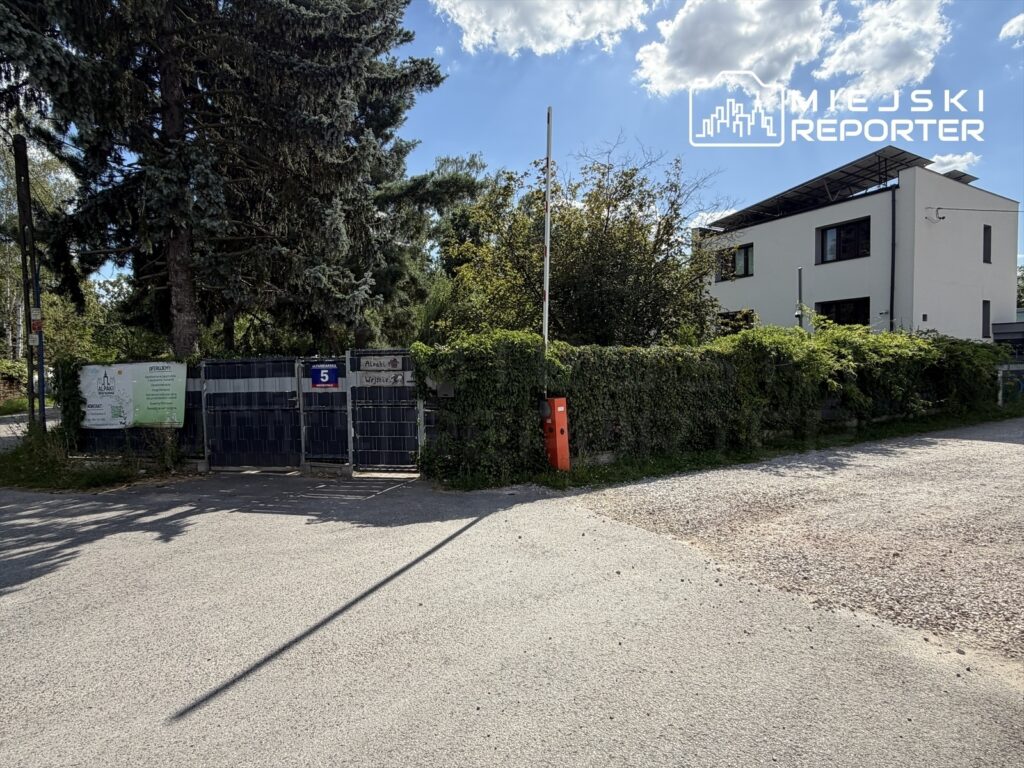Zielona brama wjazdowa prowadząca do świetlicy, otoczona drzewami i krzewami, z widocznym numerem 5.