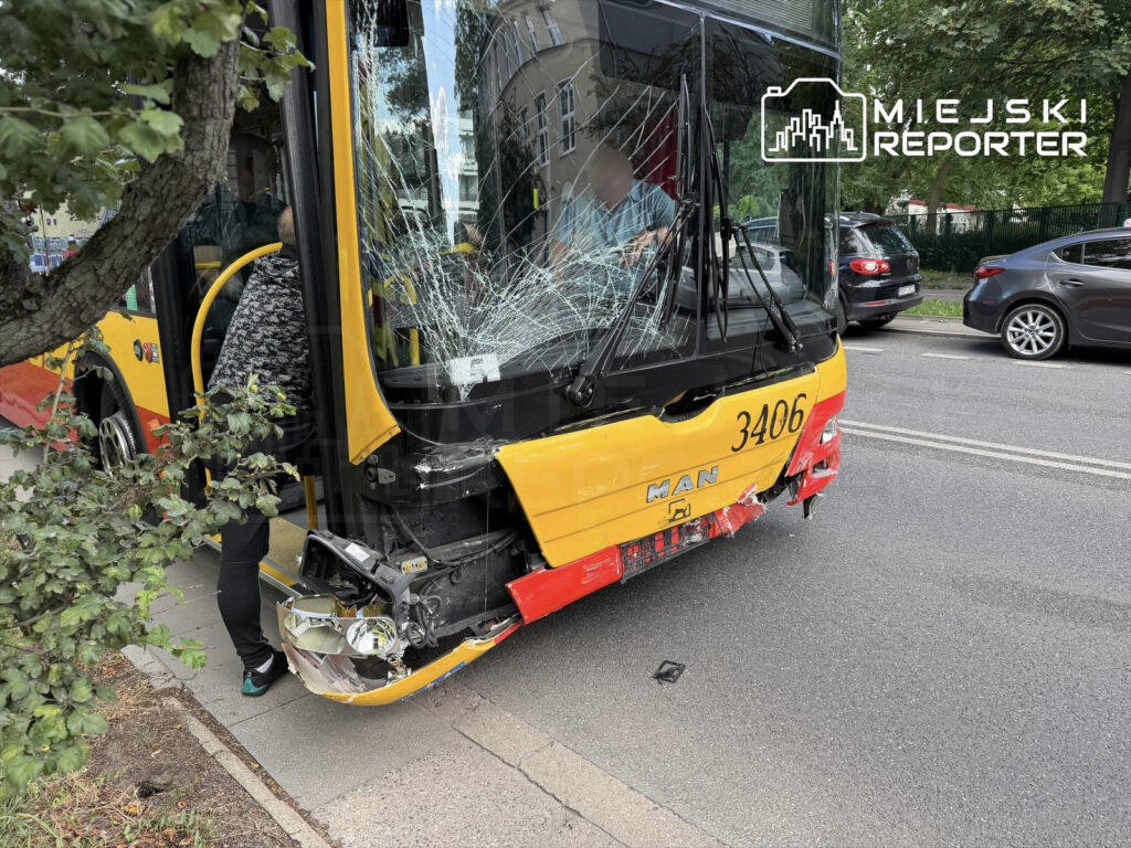 Uszkodzony autobus z rozbitym przodem stoi na ulicy, obok osoby wchodzącej do pojazdu.