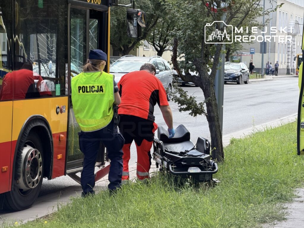 Policjantka w kamizelce odblaskowej obserwuje ratownika medycznego, który wyciąga nosze z autobusu.