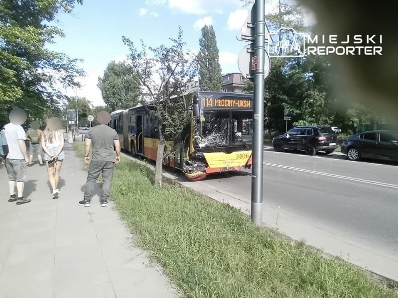 Uszkodzony autobus z numerem linii 114 stoi przy ulicy, obok spacerujących ludzi na chodniku.