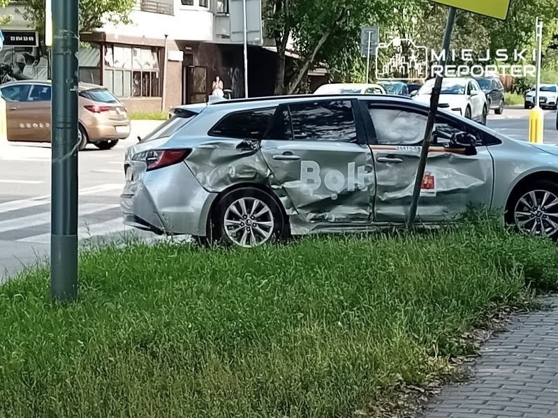 Uszkodzony samochód osobowy z widoczną wgniecioną stroną zaparkowany na trawniku obok ulicy.