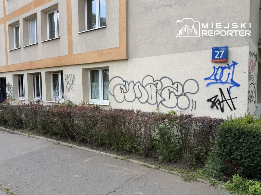 Ściana budynku pokryta graffiti, w tym napisy "2MAN JAGR BIR" oraz "LOOT", obok krzewy i chodnik. Numer domu 27.