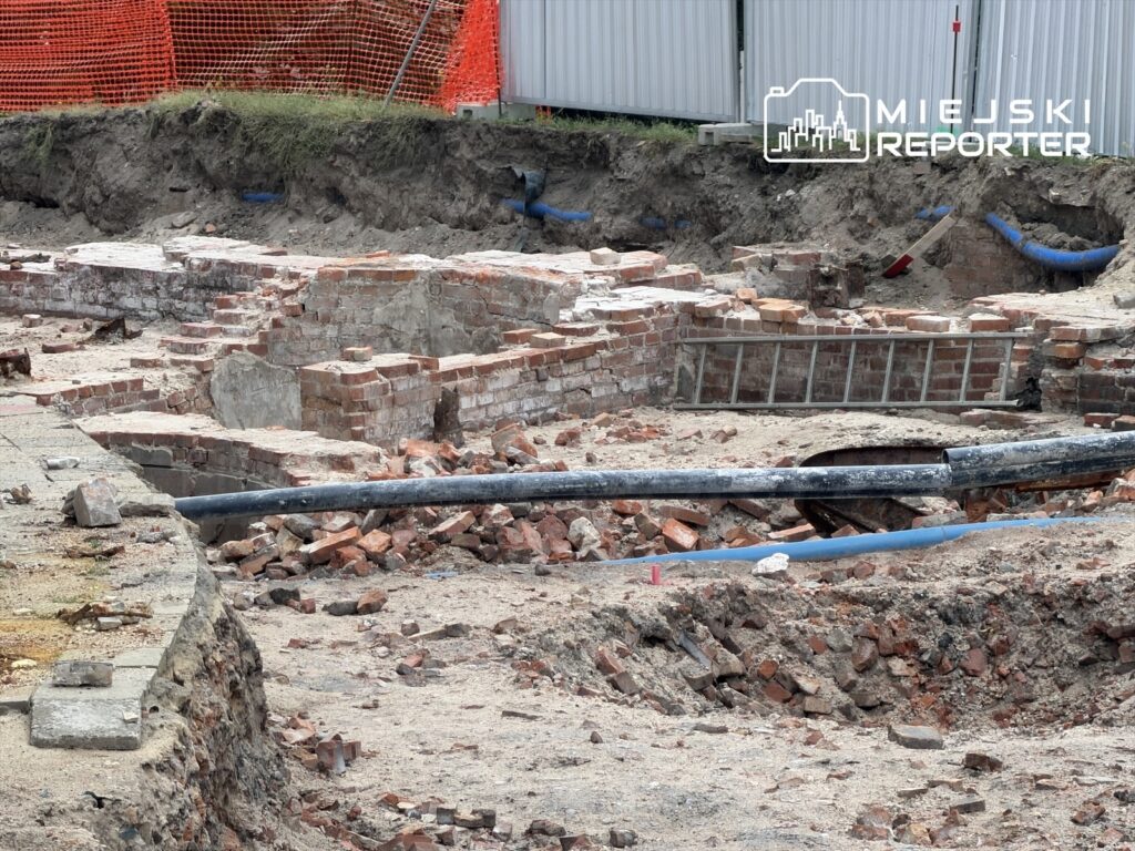 Wykopaliska ukazujące fragmenty ceglanej struktury w trakcie remontu, otoczone placem budowy i siatką ochronną.