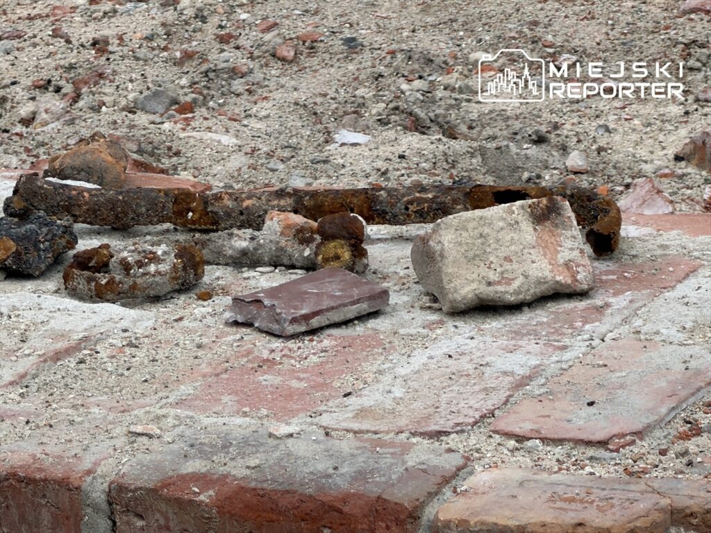 Fragmenty cegieł i metalowych elementów leżą na placu budowy, odsłaniając ślady dawnej infrastruktury.