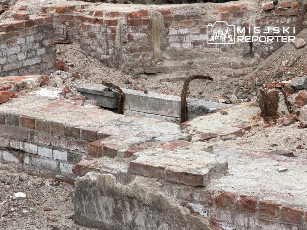 Fragment zruinej konstrukcji z cegły i betonu, z widocznymi zardzewiałymi prętami, na terenie budowy.