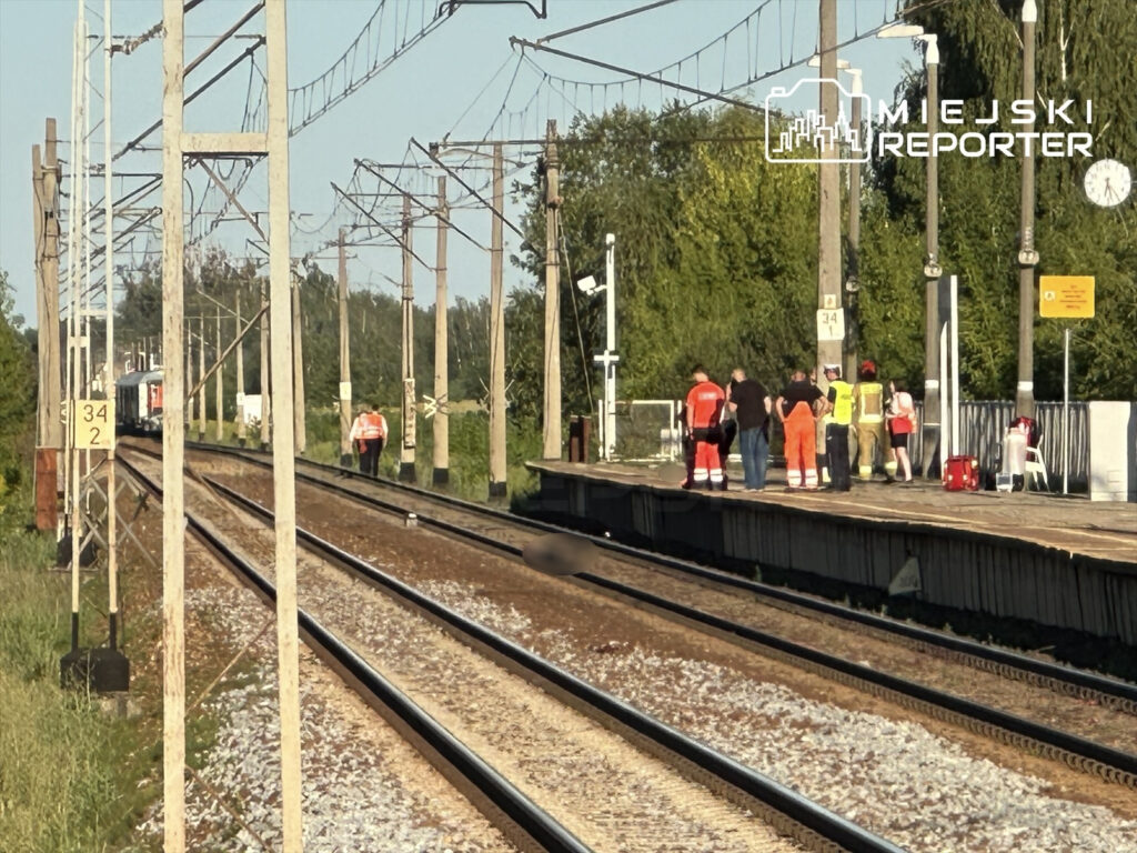 Grupa ratowników w odzieży roboczej oraz policjantów na stacji kolejowej, obok torów, gdzie doszło do tragicznego zdarzenia.