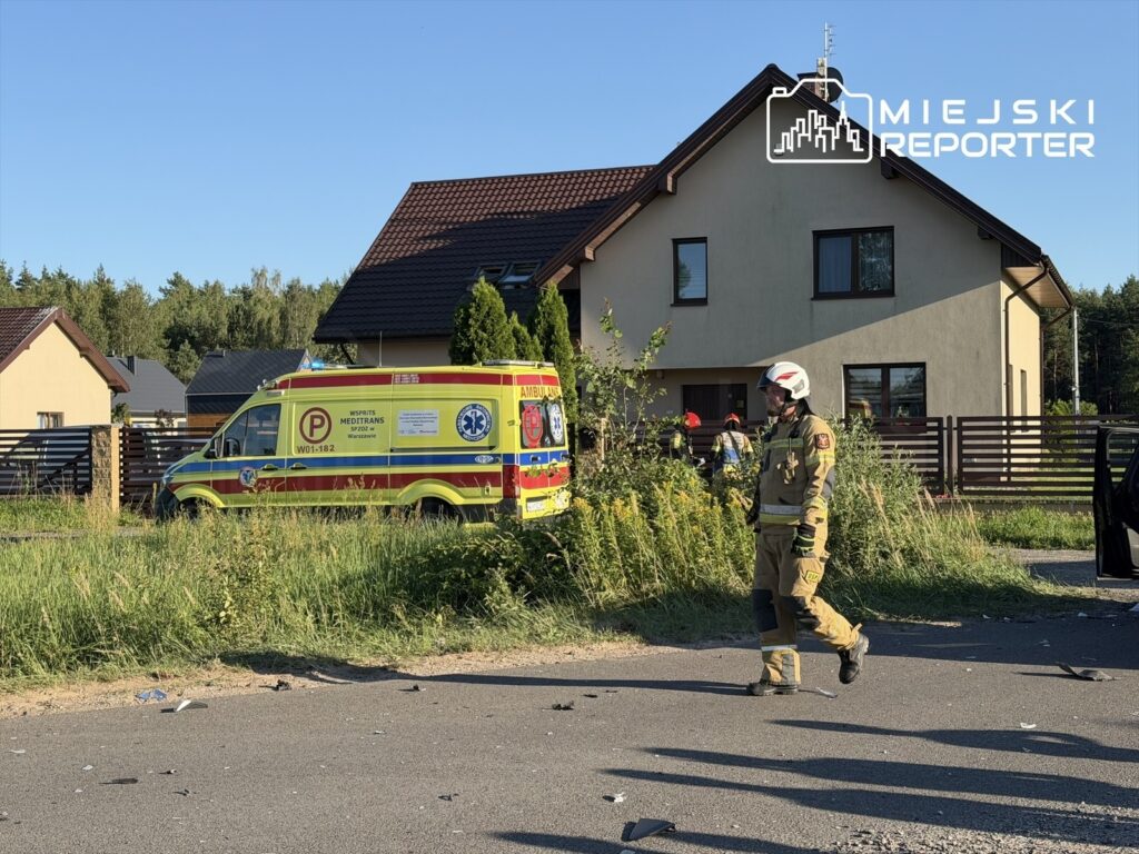 Ratownik medyczny w uniformie przechodzi obok karetki pogotowia zaparkowanej przy drodze w pobliżu domów.