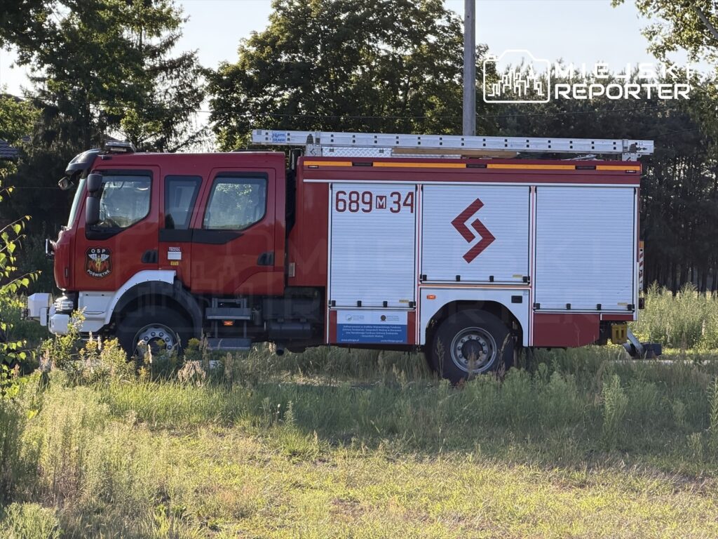 Czerwony wóz strażacki zaparkowany na trawie, z widocznym numerem 689M34 oraz logo OSP.