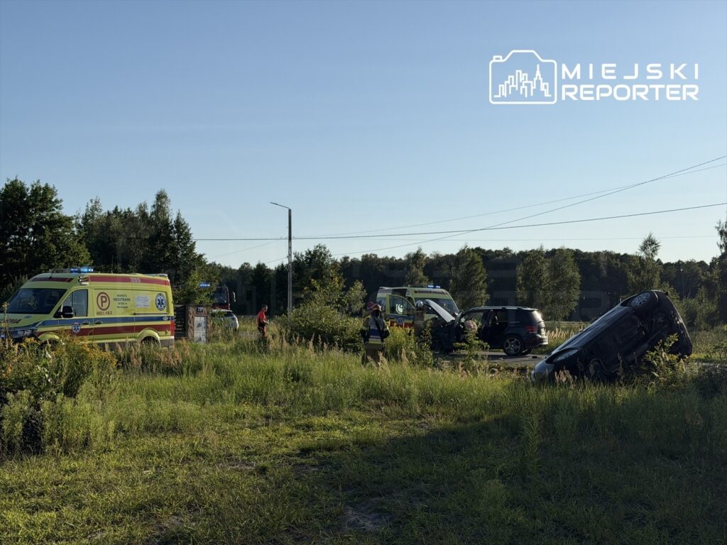 Na drodze stoją dwa karetki pogotowia, a obok przewrócone auto w przydrożnym rowie. W tle widać zieleń i drzewa.