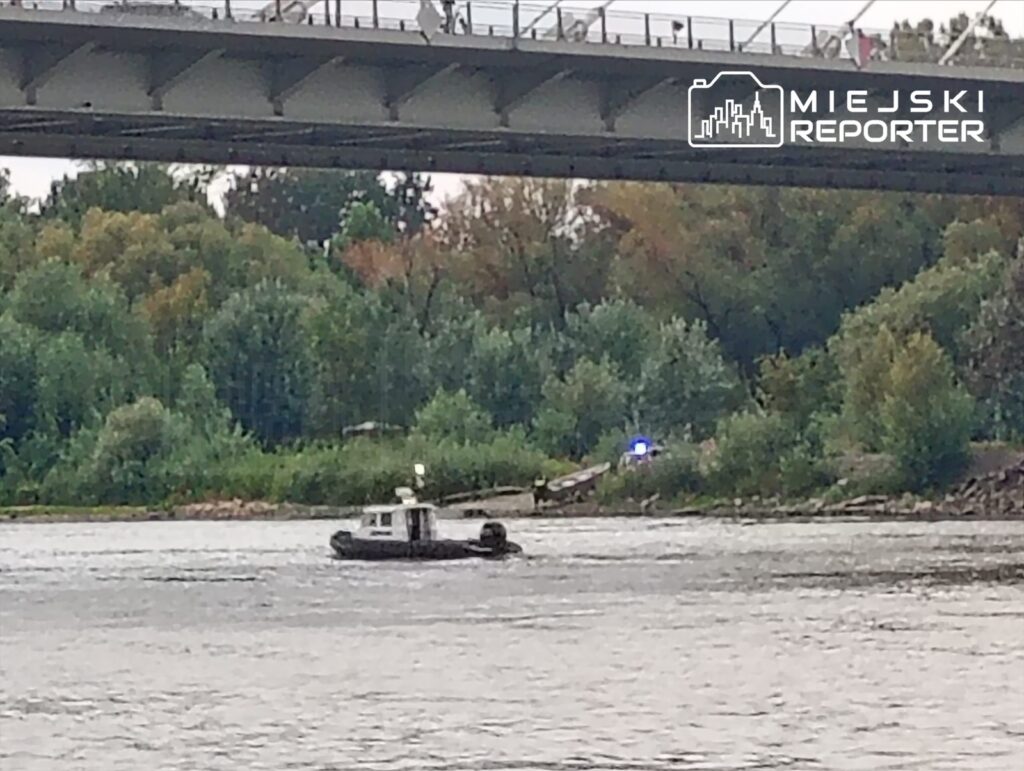 Tugboat przeszukuje nurt rzeki w poszukiwaniu zaginionego mężczyzny, w tle zarośla i most.