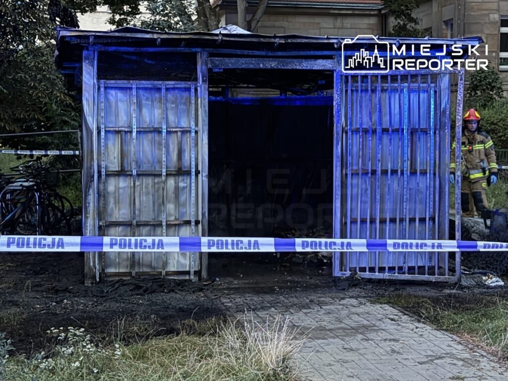Spalona altana z przeszkloną fasadą, w tle rowery, zabezpieczona taśmą policyjną; strażak przy wejściu.