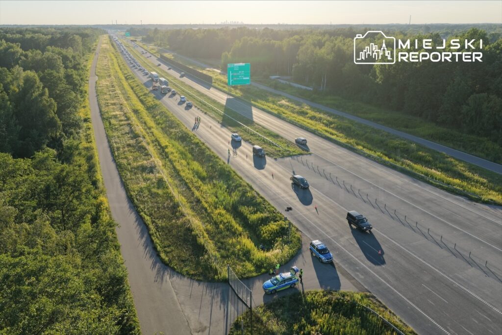 Na autostradzie A2, w miejscu zdarzenia, policjanci zabezpieczają teren w pobliżu pojazdów. W tle widać zator drogowy.