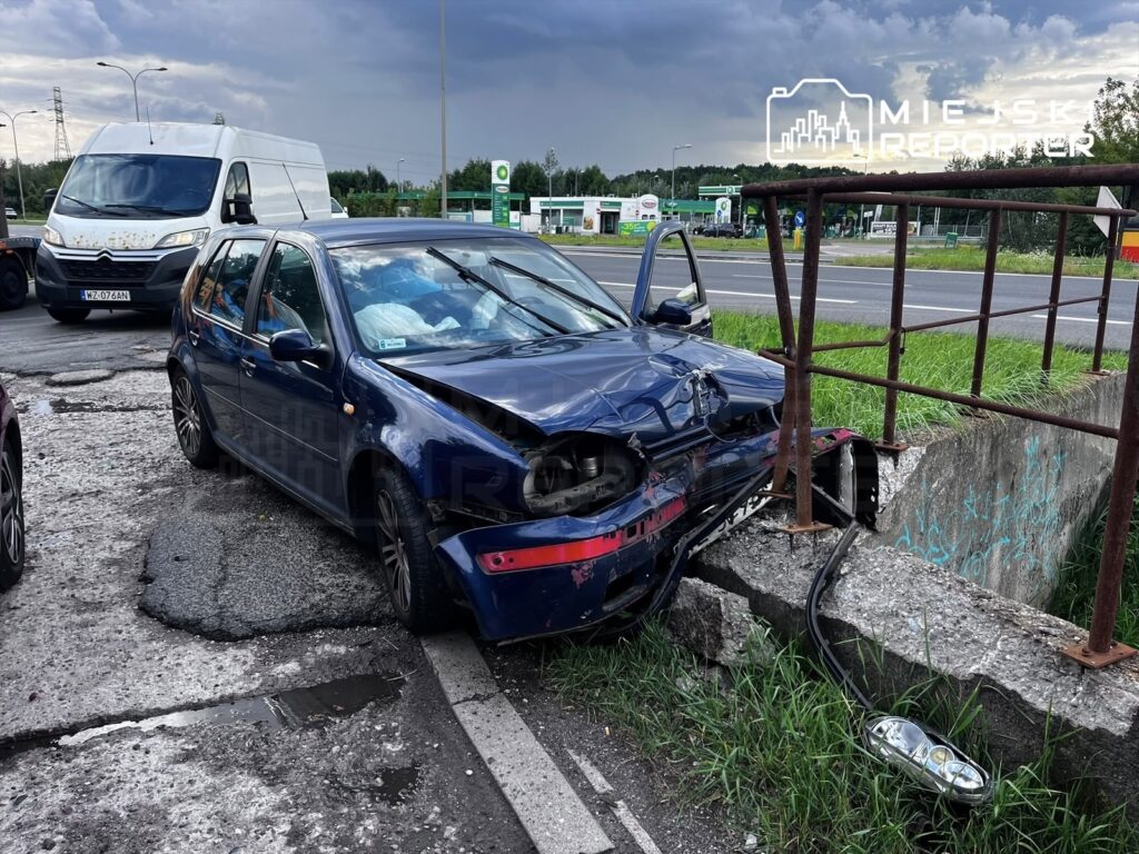 Volkswagen Golf z uszkodzoną przednią częścią wjeżdżony w betonowy przepust obok ruchliwej drogi.