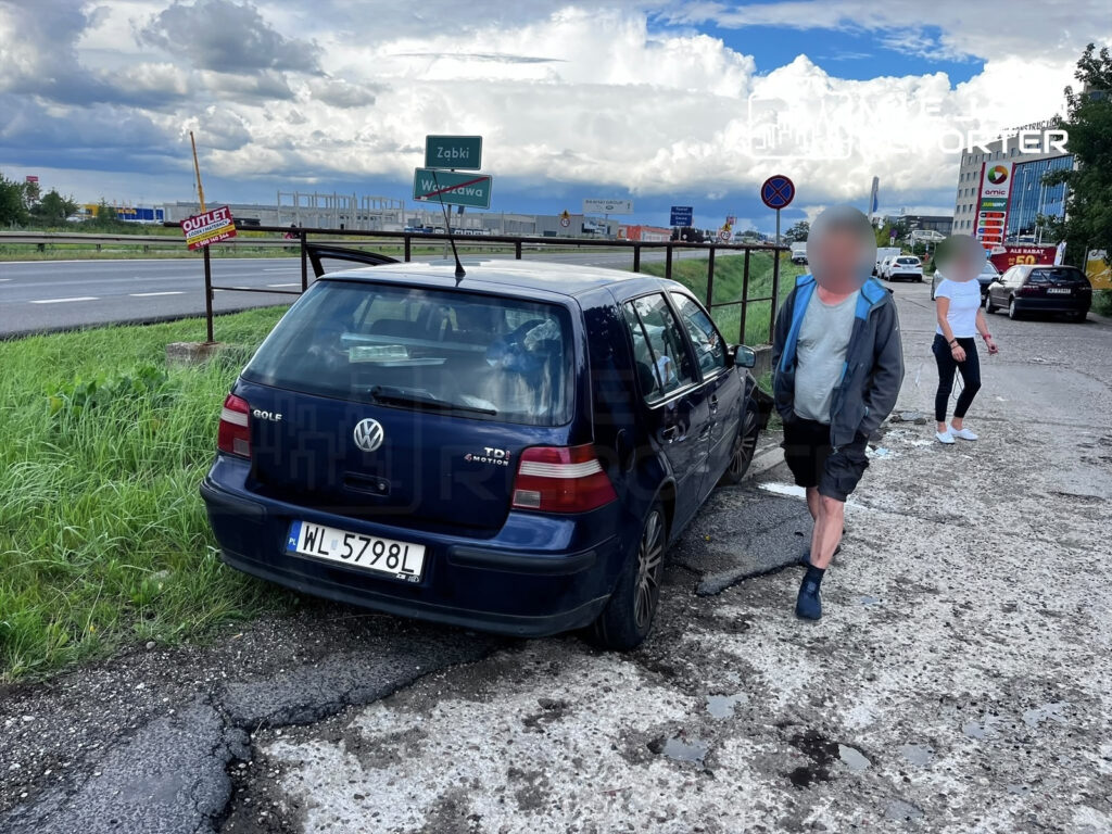 Volkswagen Golf zaparkowany na poboczu drogi, obok mężczyzna w szortach i kobieta w białej bluzce. W tle znaki drogowe.