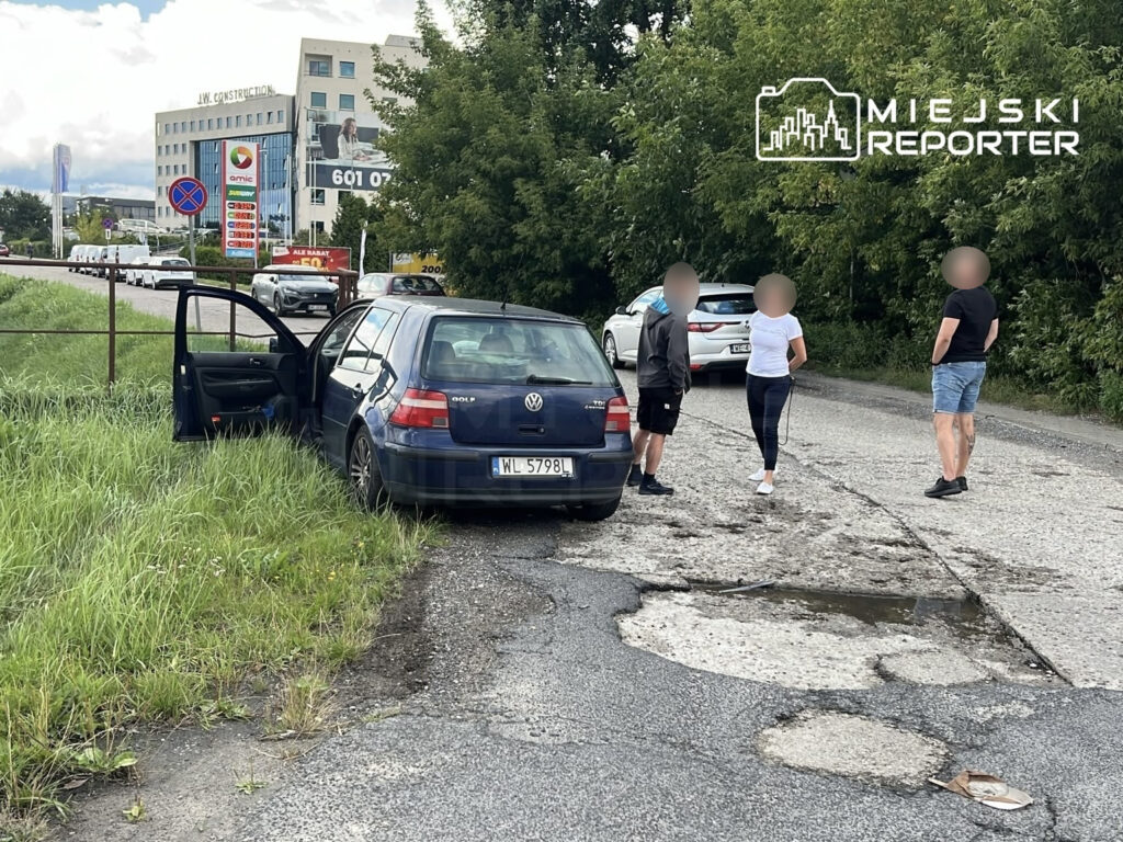 Volkswagen Golf z otwartymi drzwiami stoi na poboczu drogi, obok trzech osób rozmawiających w otoczeniu zieleni.
