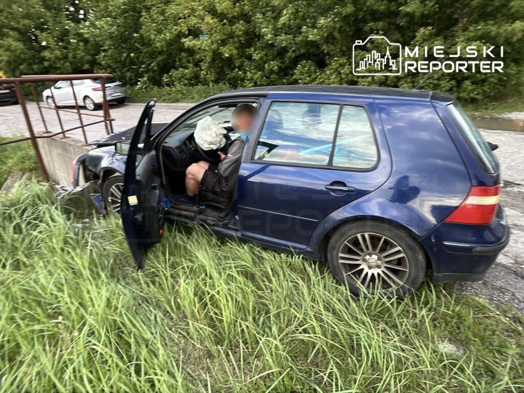 Kierowca w samochodzie osobowym z włączoną poduszką powietrzną siedzi obok betonowego przepustu w trawie.