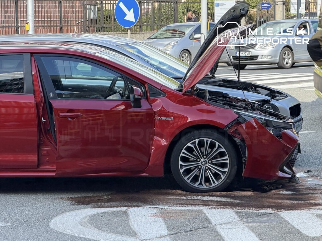 Czerwony samochód z otwartą maską stoi na ulicy, obok widoczne plamy płynów eksploatacyjnych.