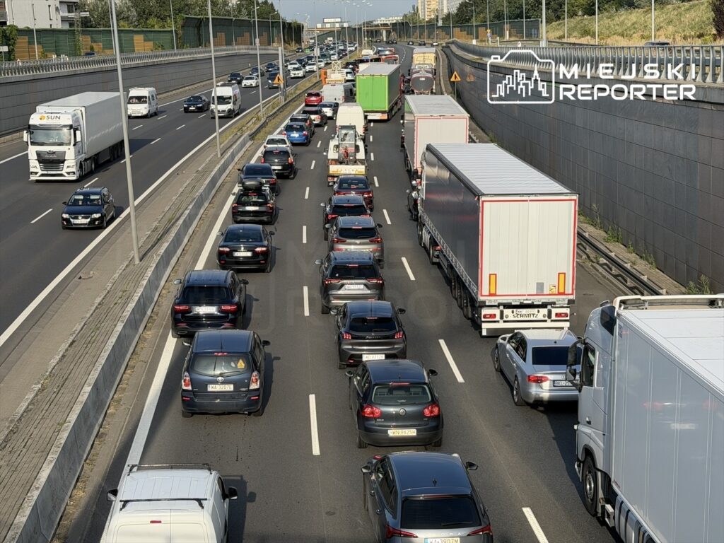 Korki na drodze ekspresowej z trzema pasami zajętymi przez stojące samochody osobowe i ciężarówki.