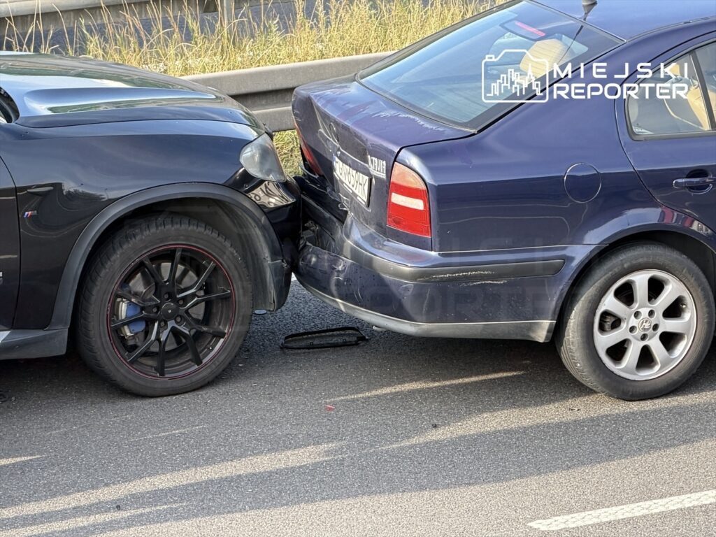 Dwa uszkodzone samochody osobowe zderzone na drodze, jeden czarny SUV z widocznymi uszkodzeniami przodu, drugi niebieski sedan z uszkodzoną tylną częścią.