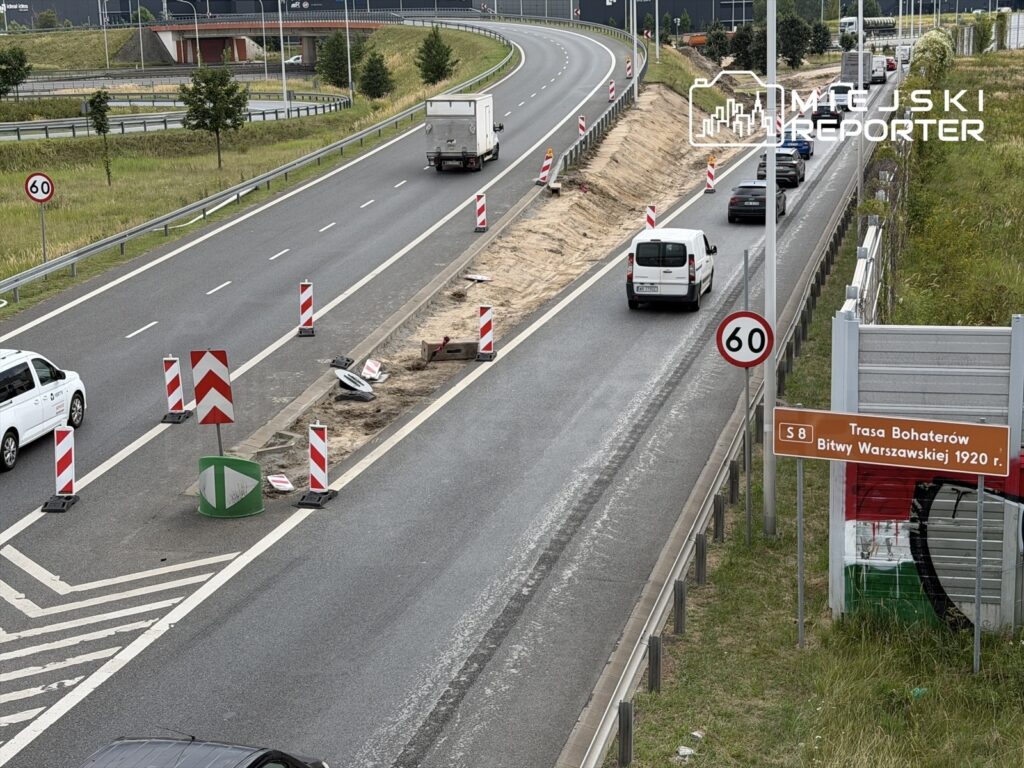 Ruch drogowy na trasie z oznakowaniem robót budowlanych, z widocznymi samochodami i znakami drogowymi.