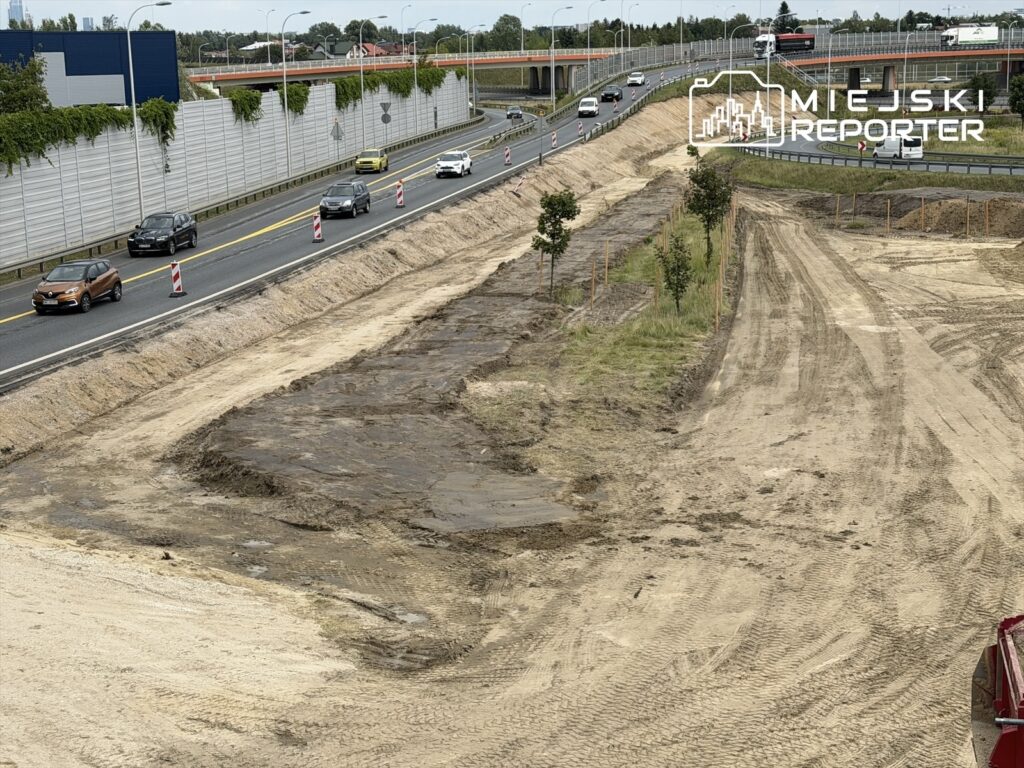 Ruch samochodowy na drodze z wyznaczonymi objazdami obok terenu budowy z usuniętą nawierzchnią.
