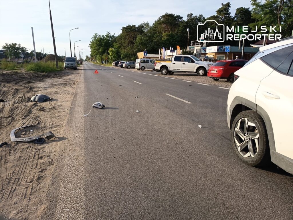 Na jezdni leżą fragmenty pojazdów, w tym zderzak i lusterko, obok widoczny trójkąt ostrzegawczy.