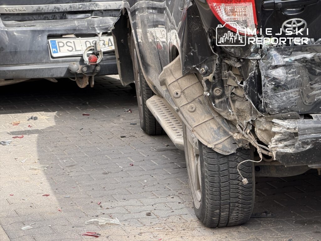 Czarne auto z uszkodzoną tylną częścią stoi na ulicy, obok szarego pojazdu, z rozbitymi kawałkami szkła na jezdni.