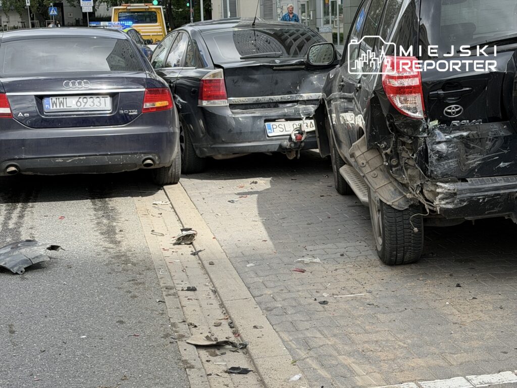 Zderzenie trzech samochodów osobowych na ulicy, w tym Audi A6 i Toyoty RAV4, z widocznymi uszkodzeniami nadwozia.