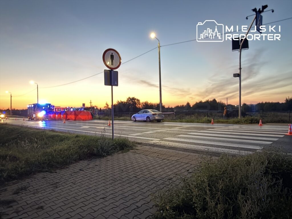 Na drodze z widocznymi służbami ratunkowymi oraz czerwonymi namiotami zabezpieczającymi, w tle zachód słońca.