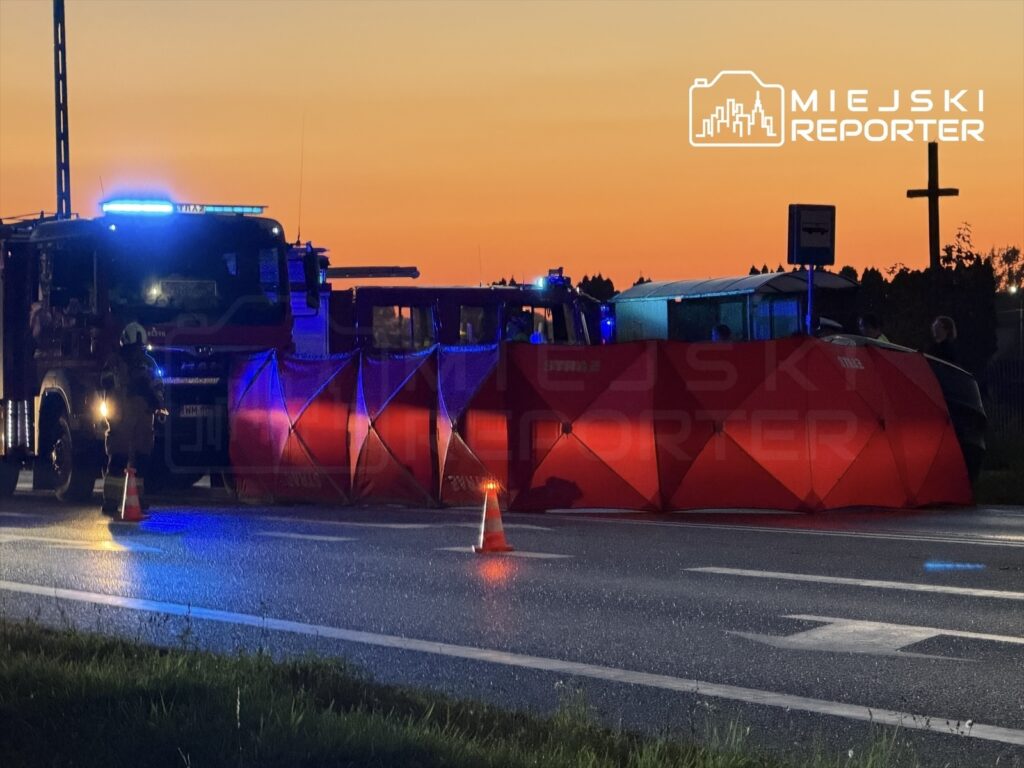 Na drodze ustawione są namioty zabezpieczające, w tle widać wozem strażackim i zachód słońca.