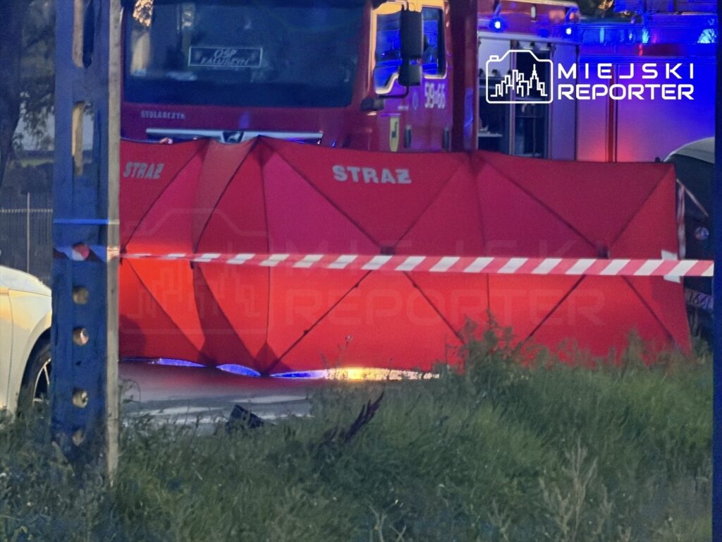 Czerwony namiot strażacki ustawiony obok drogi, z widocznymi oznaczeniami "STRAŻ" i policyjnym taśmą zabezpieczającą.