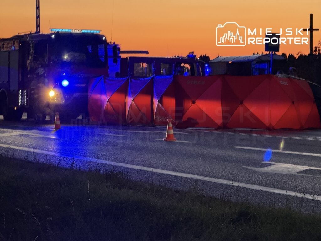 W nocy na drodze stoi wóz strażacki z włączonymi sygnalizatorami, obok rozstawione czerwone namioty.