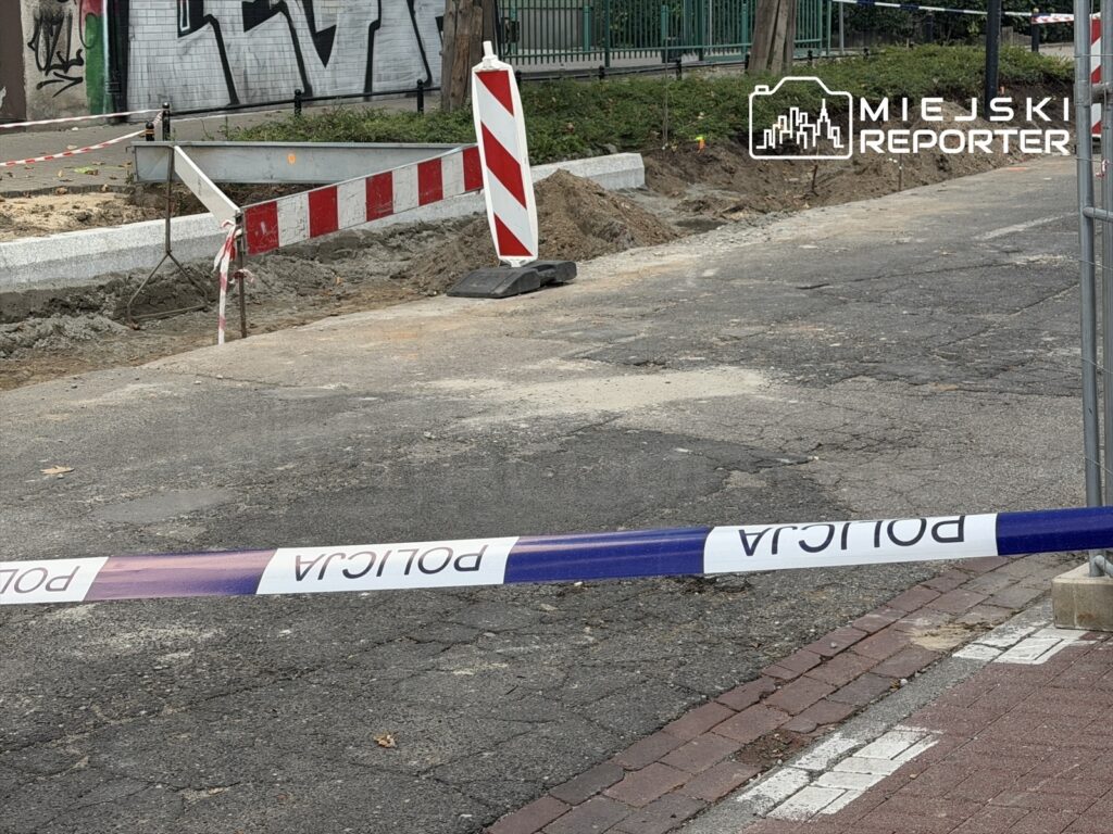 Na drodze znajdują się oznaczenia budowy, a w tle widoczny jest mural na ścianie.