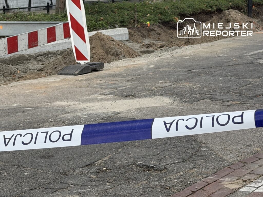 Roboty drogowe na ulicy, z widoczną taśmą policyjną i oznakowaniem zakazu wstępu. W tle widoczny wykop.