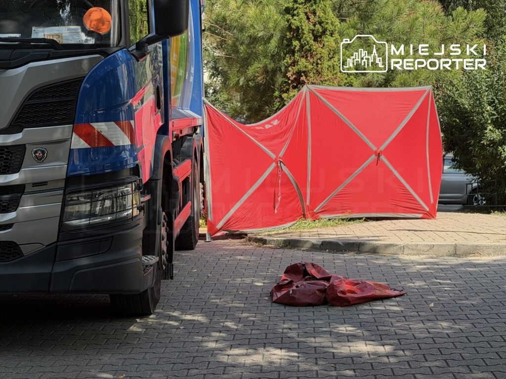 Niebieski samochód ciężarowy zaparkowany obok czerwonego namiotu w miejskim otoczeniu, na kostkowanej nawierzchni.