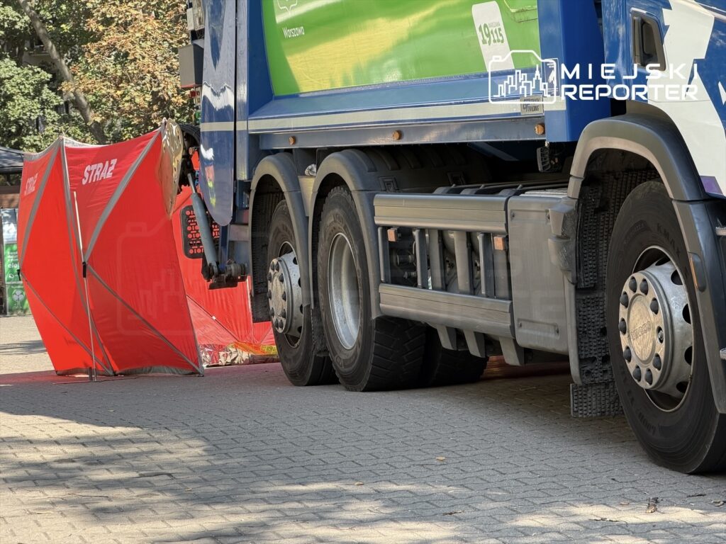 Czerwony namiot strażacki ustawiony obok dużego, niebieskiego śmieciarki na chodniku w słoneczny dzień.