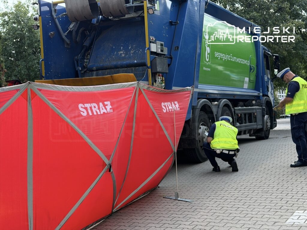 Funkcjonariusze policji sprawdzają stan techniczny śmieciarki, a obok ustawiona jest czerwona bariera z napisem "STRAŻ".