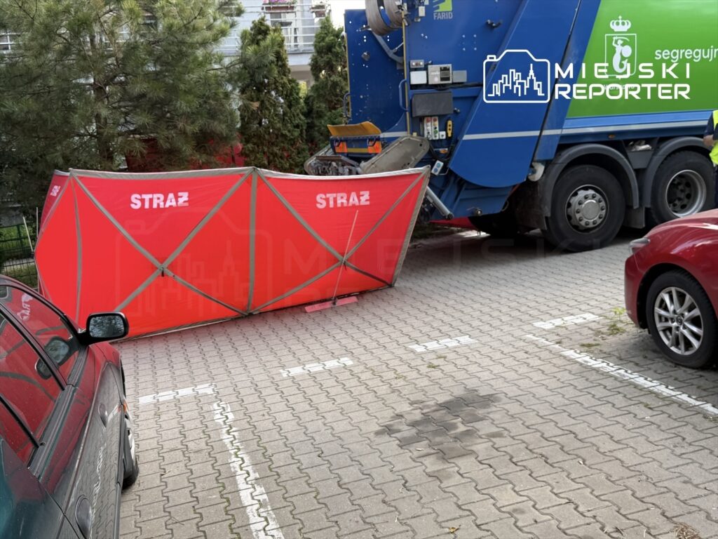 Czerwony namiot z napisem "STRAŻ" ustawiony obok niebieskiego samochodu ciężarowego na parkingu.