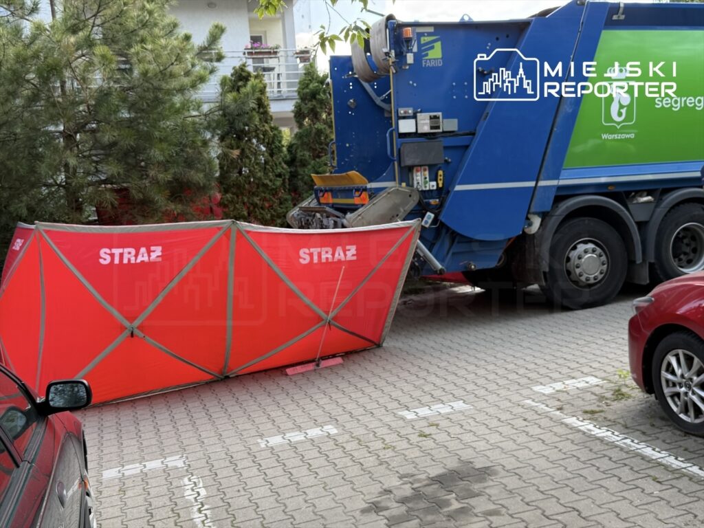 Czerwony namiot oznaczony napisem "STRAŻ" ustawiony obok niebieskiego pojazdu śmieciarki na parkingu.