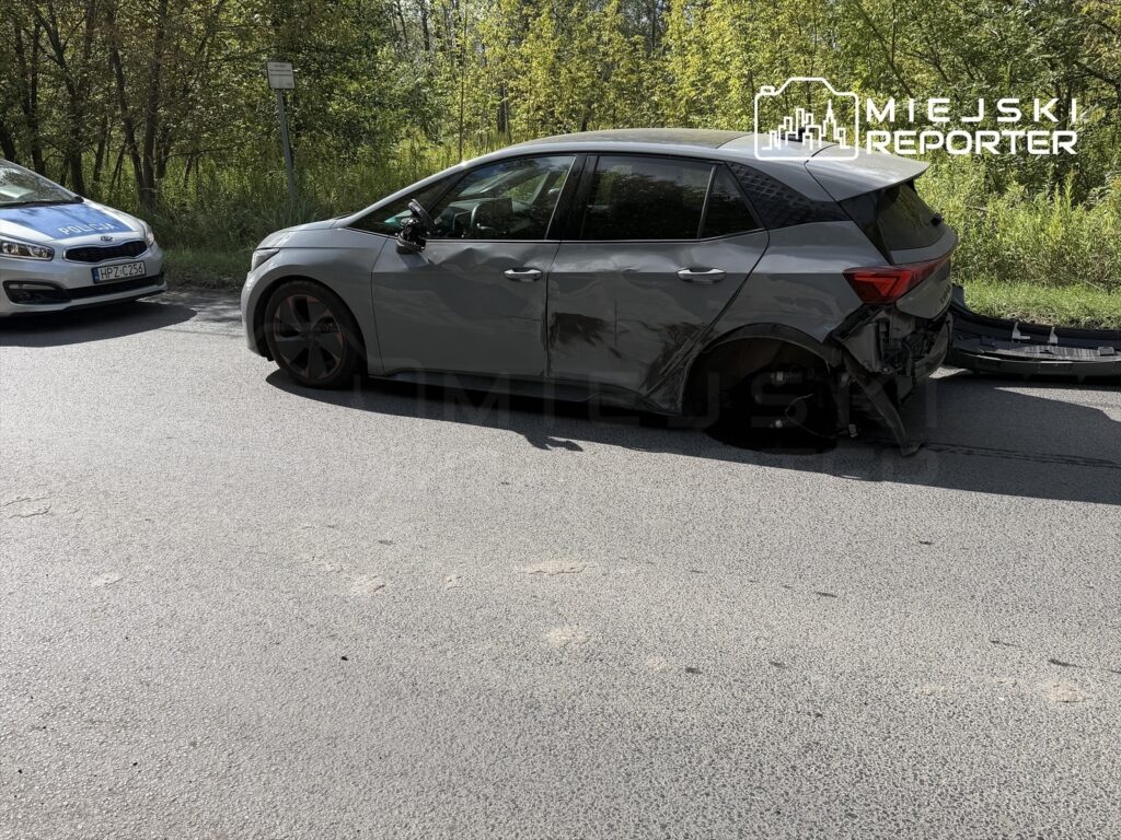 Uszkodzony samochód osobowy z zarysowaniami na boku stoi na drodze, obok policyjny radiowóz.